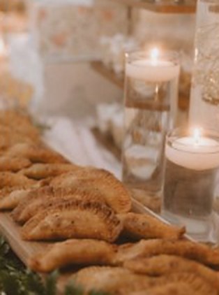 A tray of golden empanadas beside candles at an event